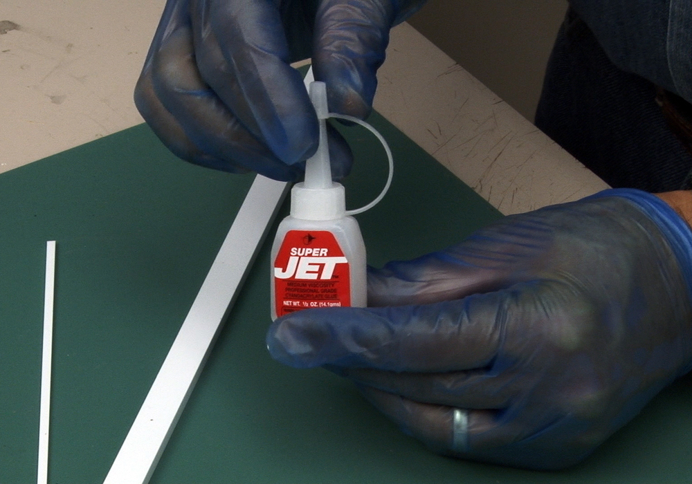 Rubber-gloved hands holding a small bottle of JET CA glue.