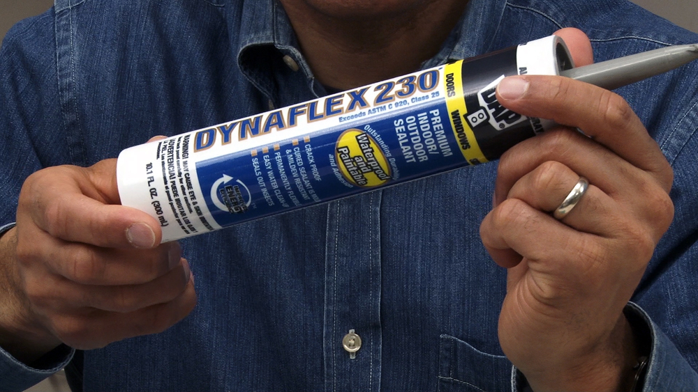 Producer's hands holding a tube of construction adhesive, face not visible