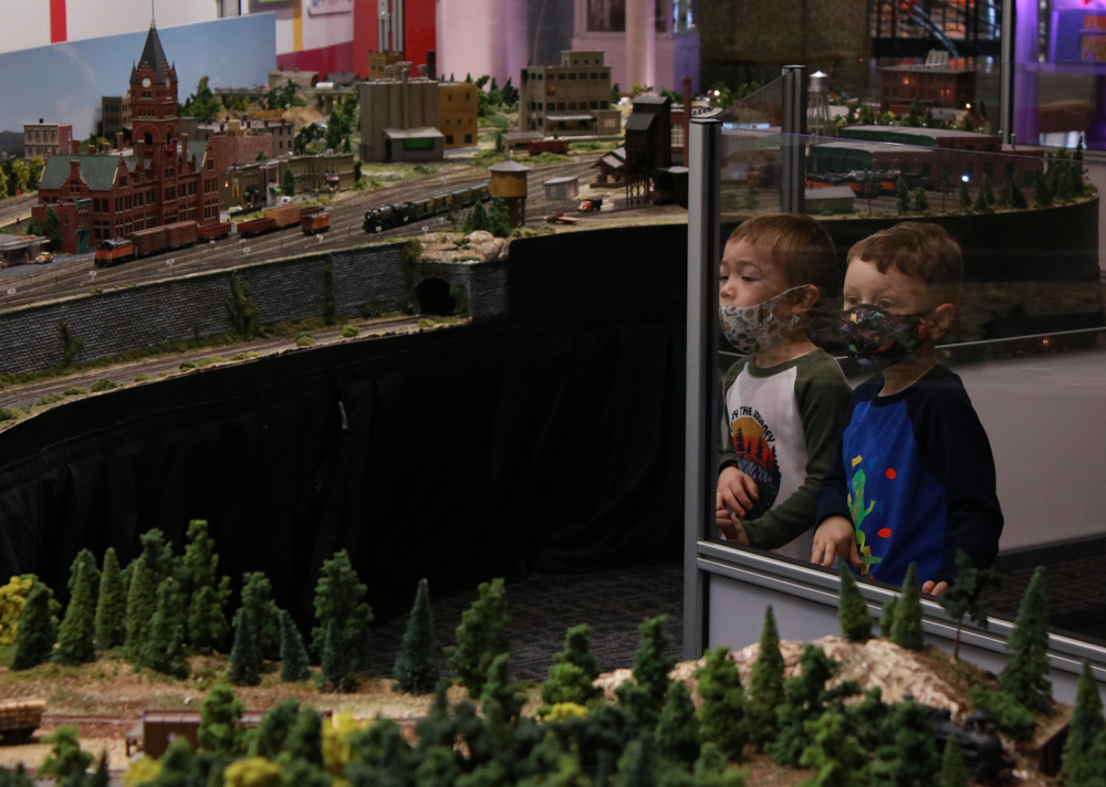 Two young boys leaning on plastic in front of train exhibit.