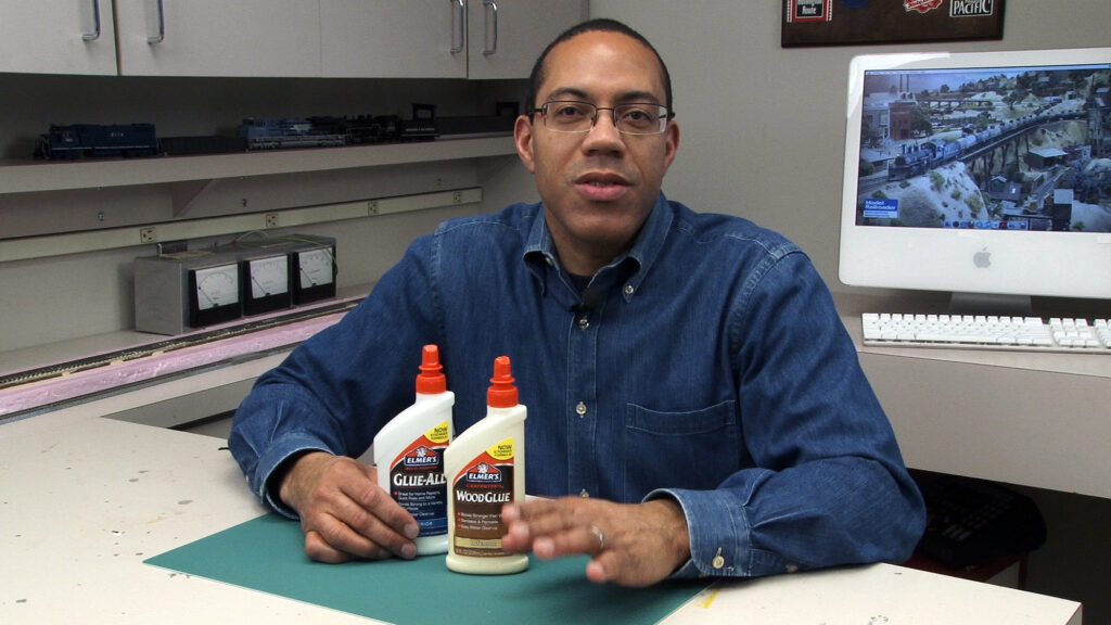 rains.com producer holding glue bottles and talking to camera at a workbench