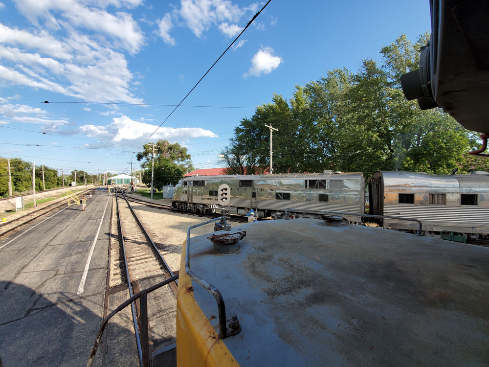 silver streamlined passenger train makes way toward mainline tracks