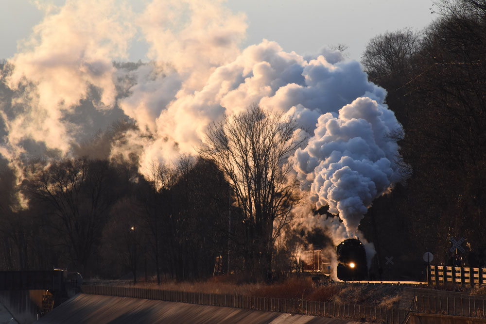 Predawn light illuminates the large plume as steam engine pulls train