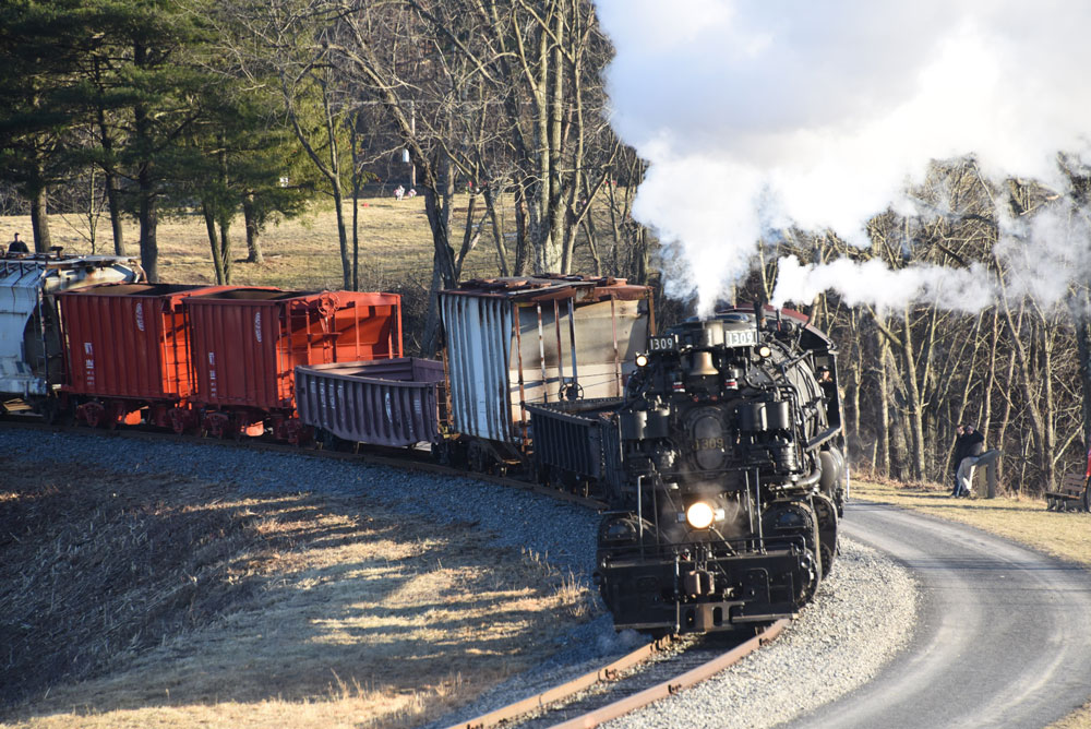 Black steam engine with photo freight comes around a horseshoe curve