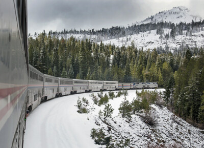Front of an Amtrak train as seen from the rear in a snowy mountain landscape. Trains LIVE — Riding Amtrak.