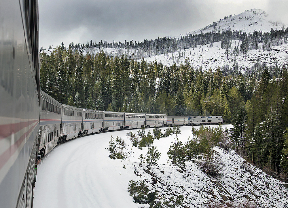 Front of an Amtrak train as seen from the rear in a snowy mountain landscape.