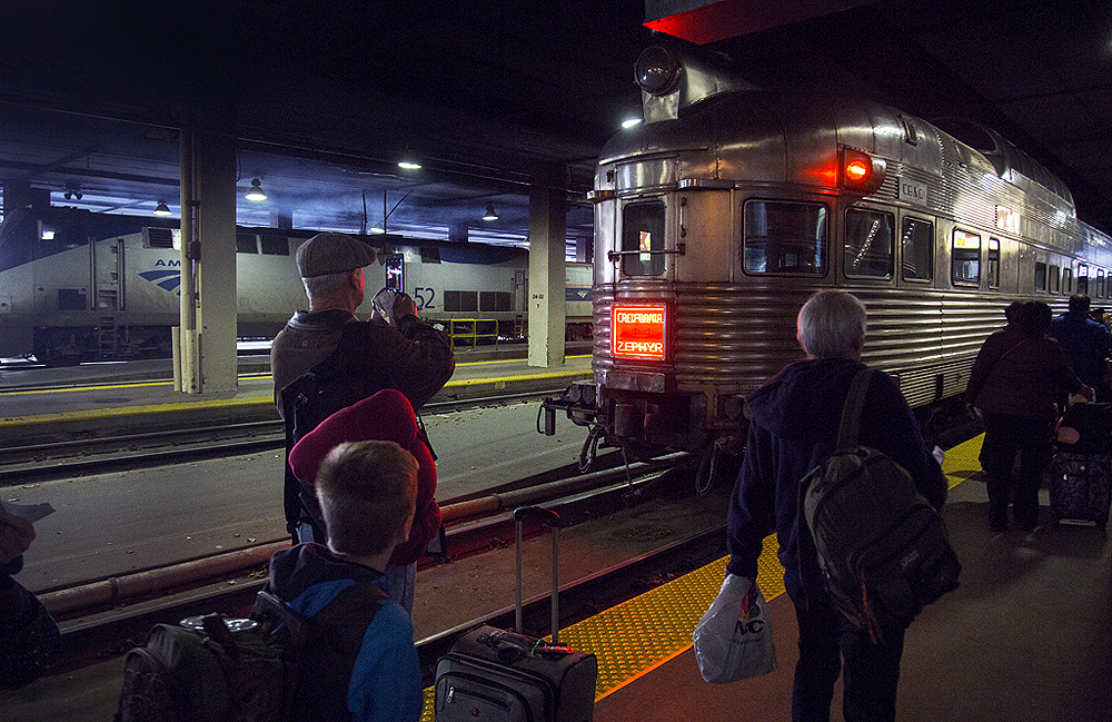 People in a dark train shed take picture of a streamlined passenger car.