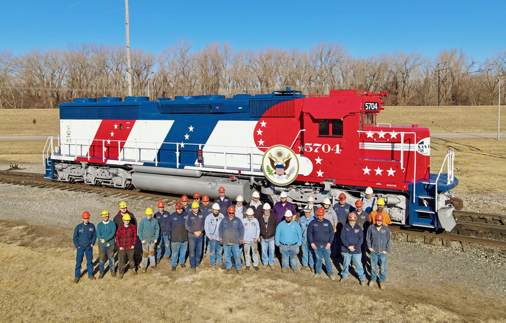 A group of people pose in front of a red, white, and blue locomotive
