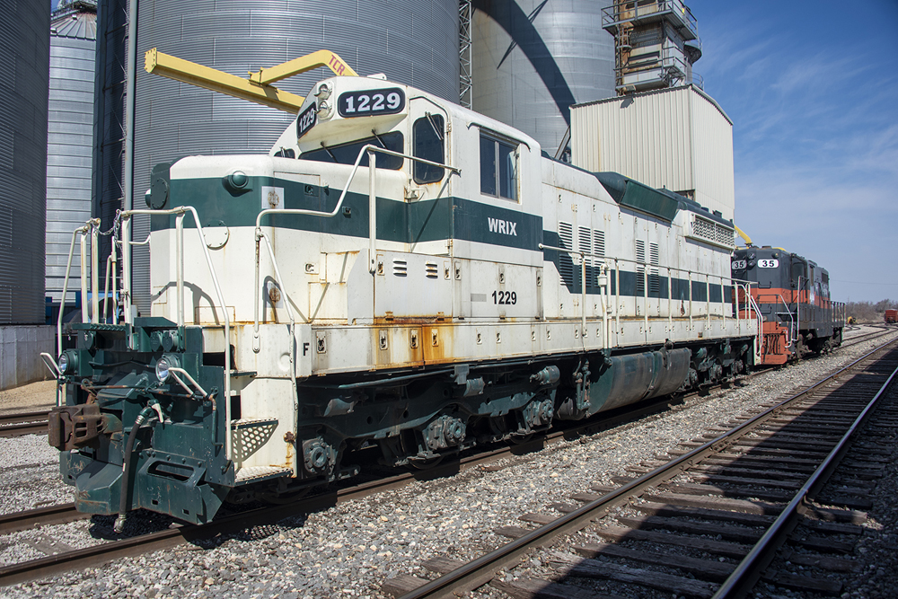 White locomotive with green stripe, with gray and orange locomotive behind