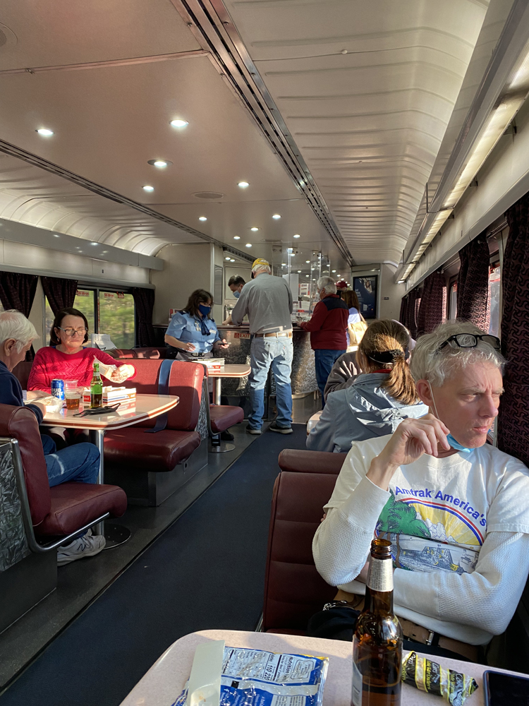 Passengers in lounge car, with some standing at counter to purchase food and beverages