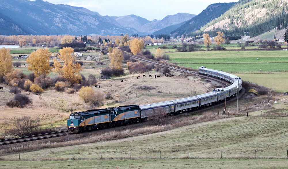 Long passenger train crounds curve in mountain valley