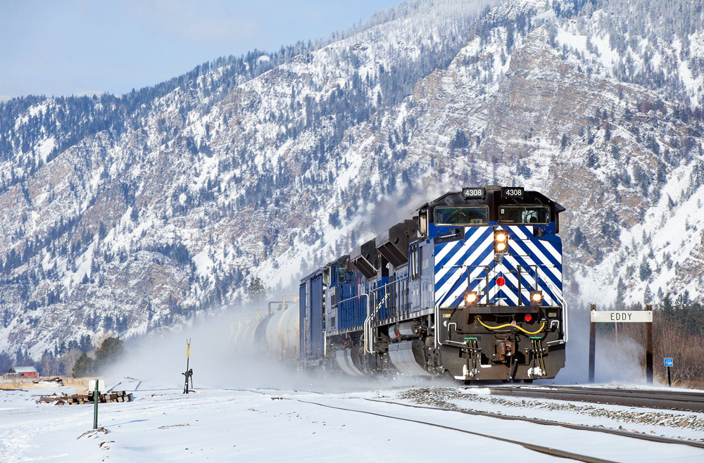 Blue and white locomotives on train in mountains covered with snow under blue skies