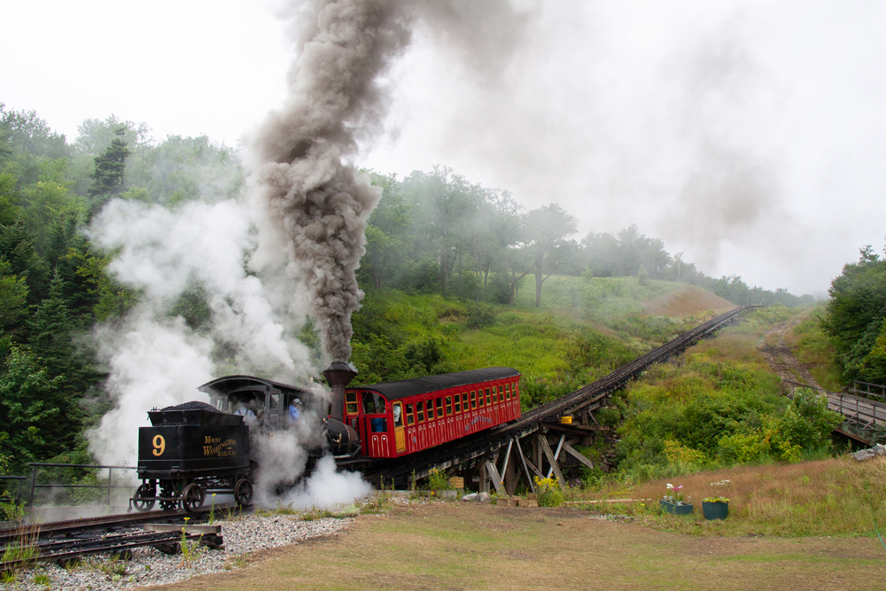 Steam locomotive pushing railroad car up steep grade
