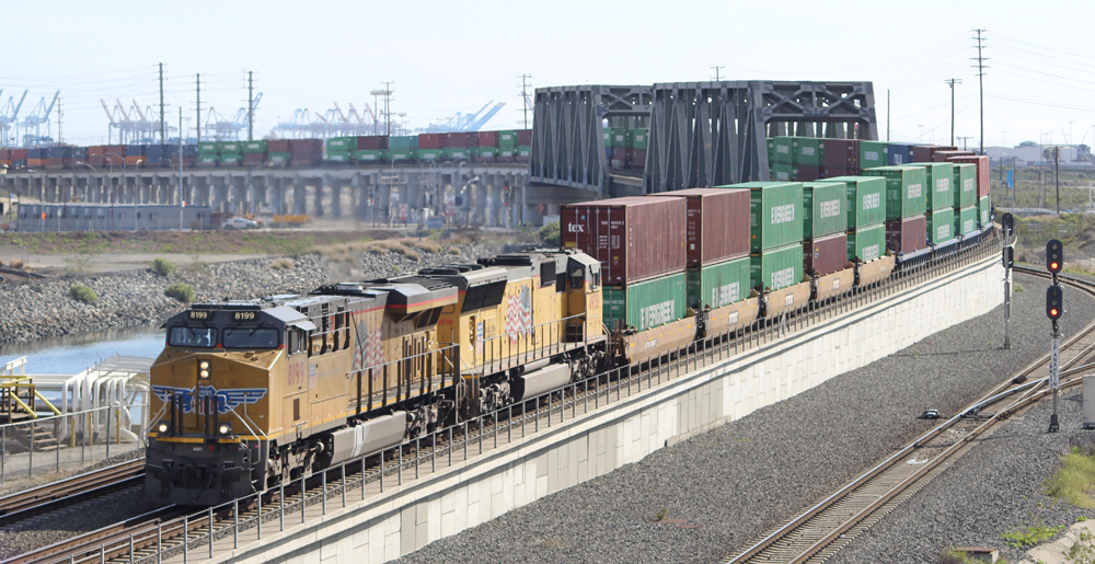 Yellow locomotives leading train of double-stacked containers over bridge