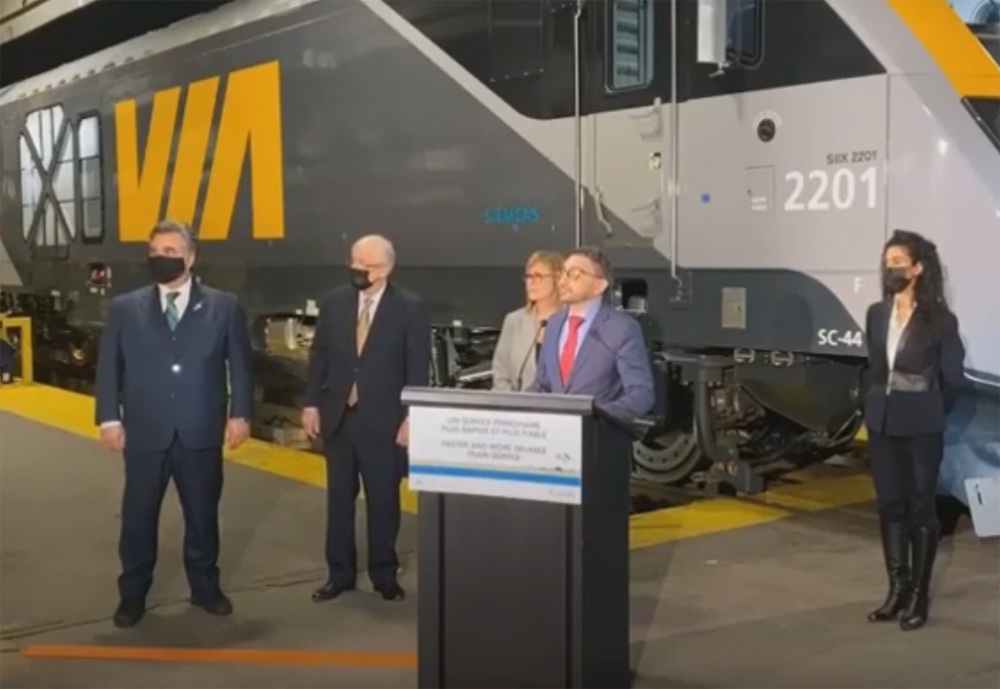 Man speaking at podium in front of locomotive