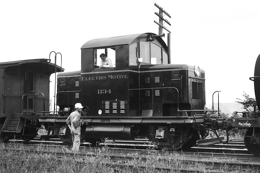 Men look at EMD Model 40 centercab diesel locomotive coupled to train cars