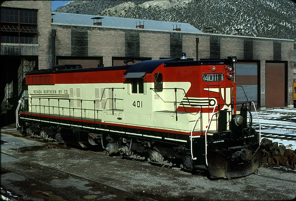 Red and cream-painted diesel locomotive in front of a rail shop.