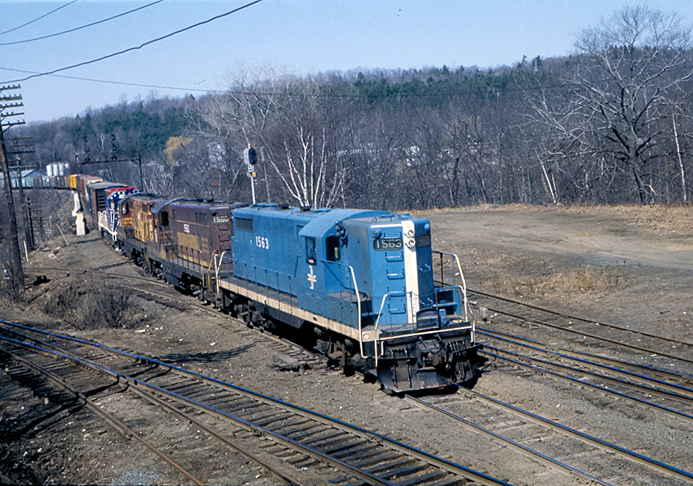 1950s EMD customer relations: A blue-painted locomotive leading a freight train in a barren-tree landscape.