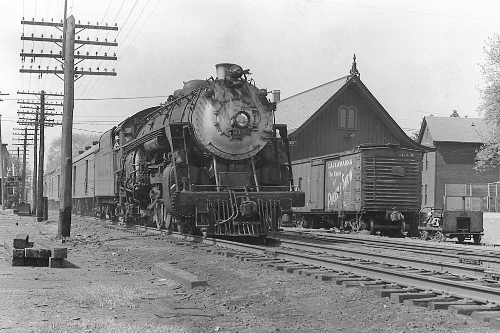 Black and white image of a steam locomotive passing a depot.