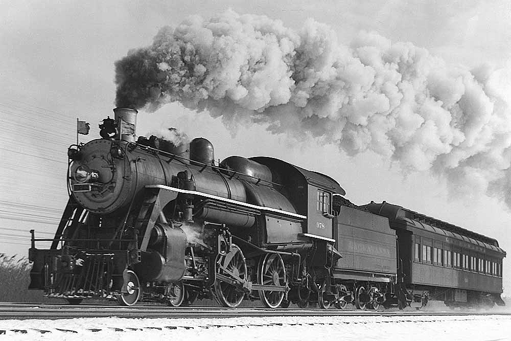 Steam locomotive with passenger train in a black and white image.
