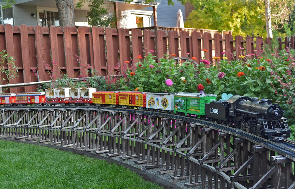 Model steam train on wood trestle with zinnias in background