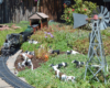 Model steam train approaches curve with cows and windmill nearby