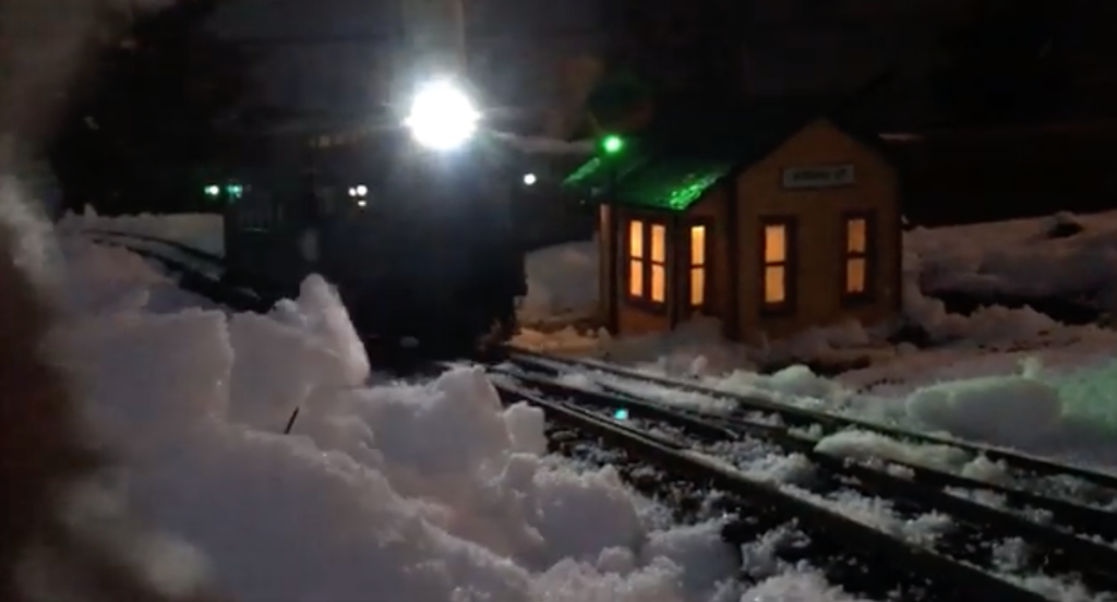 Snowy garden railway with lit train approaching