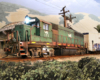 A rusty green diesel is seen in low angle pulling a graffiti-covered reefer car past fruit groves