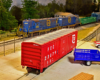 A bright red boxcar sits in a paved lot next to a blue stakebed truck while a train passes behind