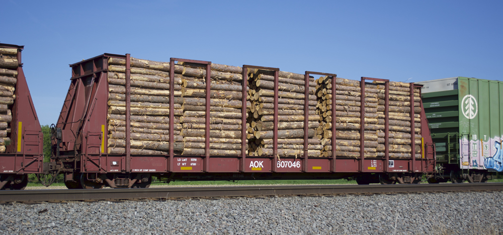 Photo of flatcar painted Oxide Red with side stakes and pulpwood load.