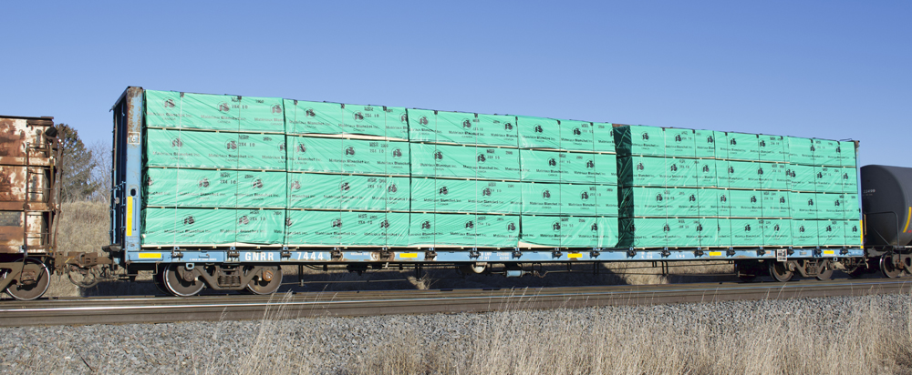 Modeling freight car loads: Photo of blue flatcar with wrapped lumber load.