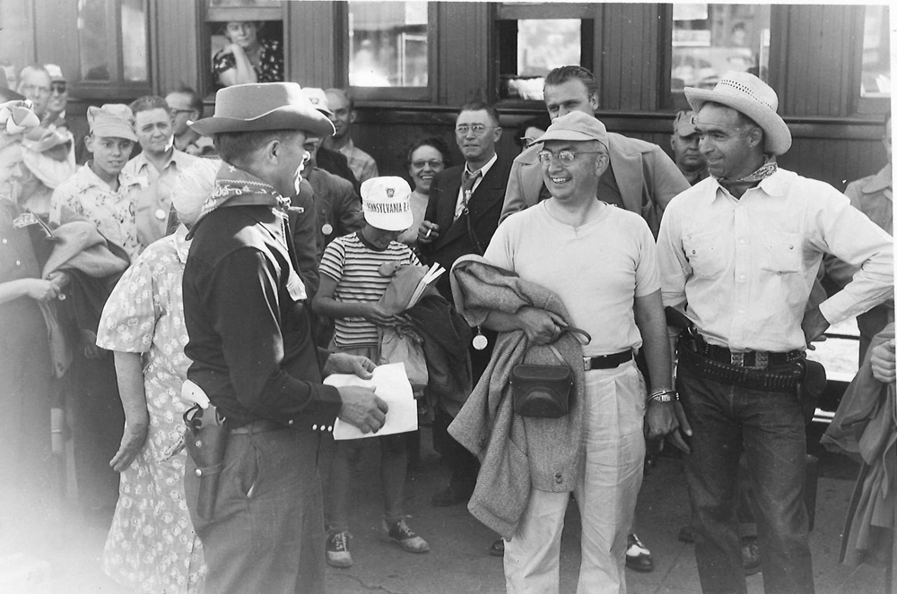 Men smiling and talking surrounded by a group of people gathered at a convention