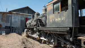 black steam locomotive sits outside enginehouse