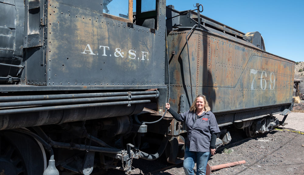 woman stands next to black steam locomotive