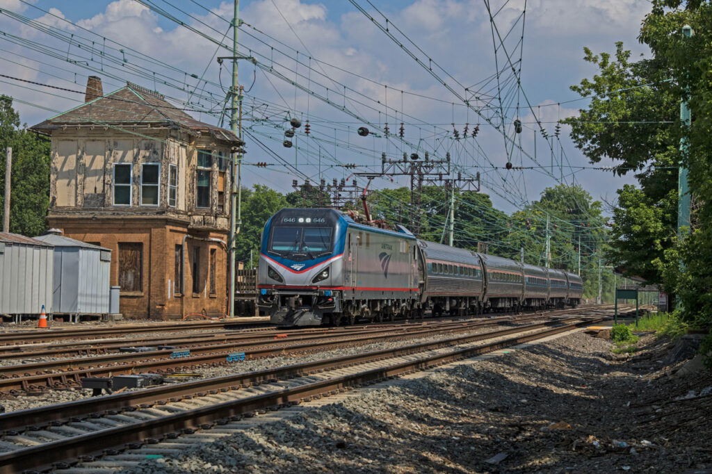 blue and silver passenger train passes brick tower