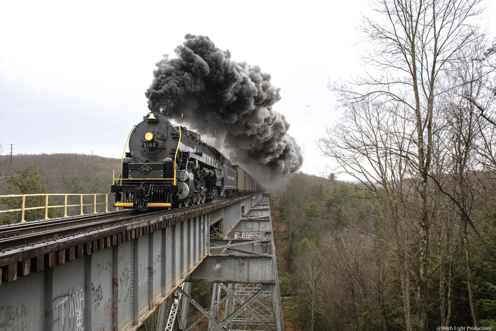 Steam locomotive spewing black smoke while crossing bridge