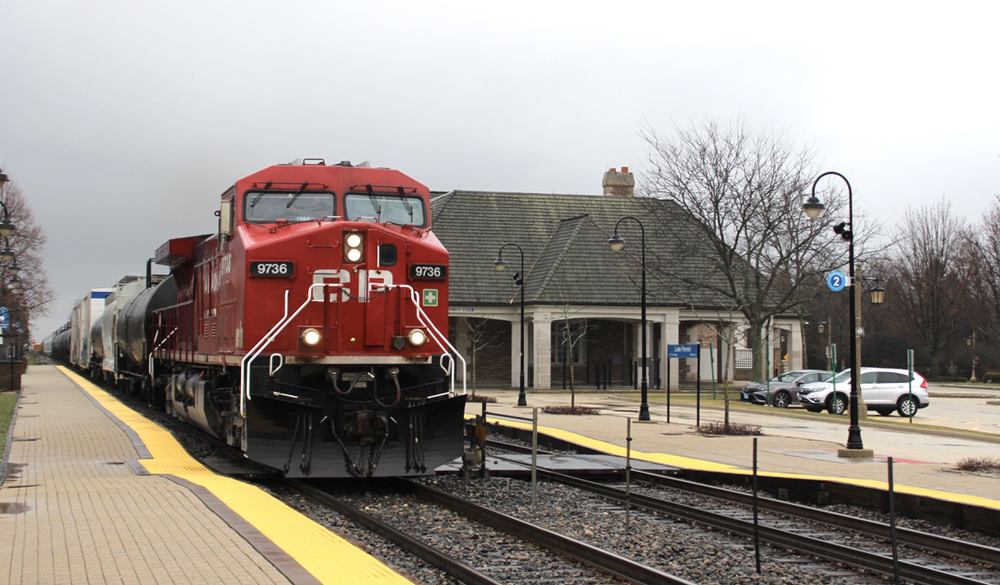 Red locomotive leads train past passenger station