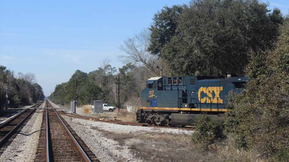 Blue and yellow locomotive waiting on siding, as seen from train on main line