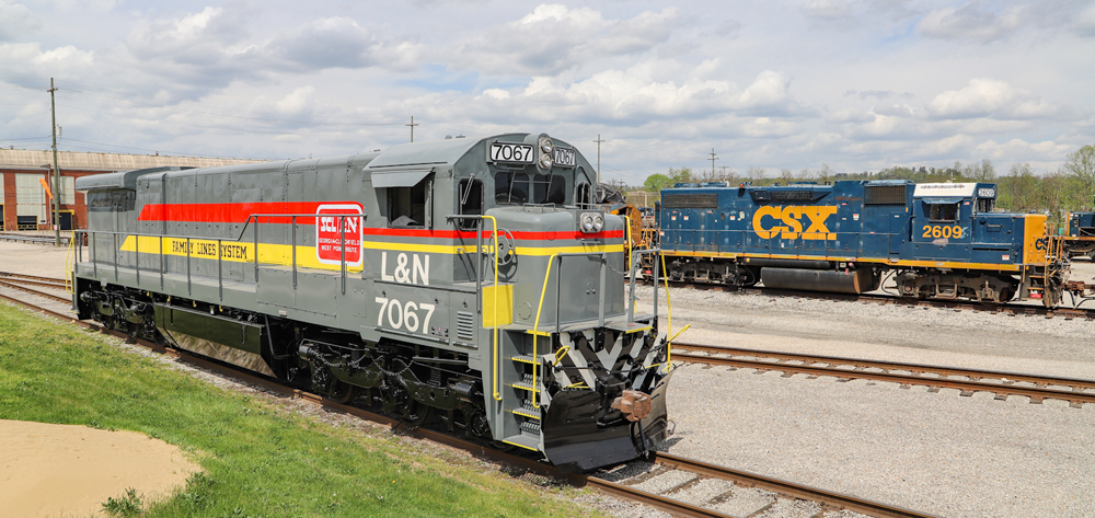 Gray locomotive next to blue locomotive outside shop building