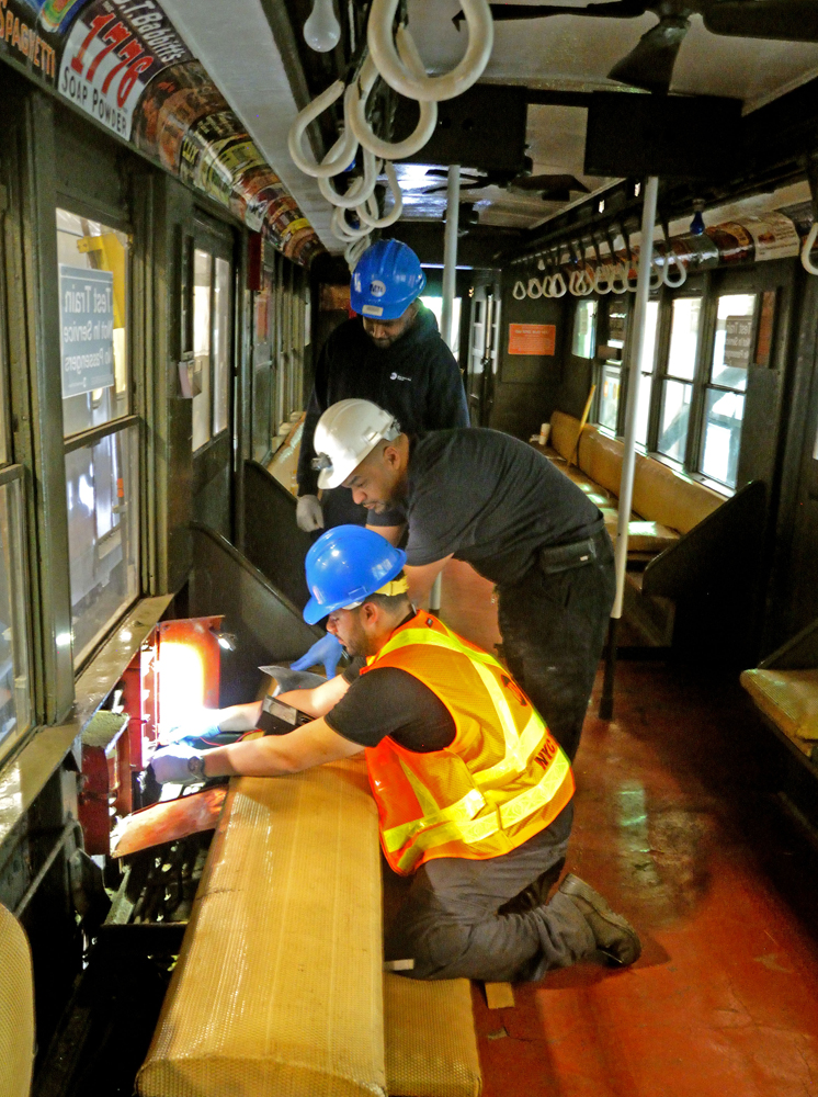 Three men work inside vintage subway car
