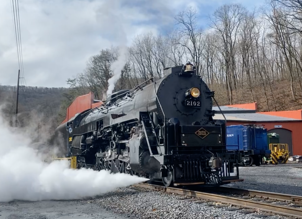 Large, black steam locomotive under power and steaming.