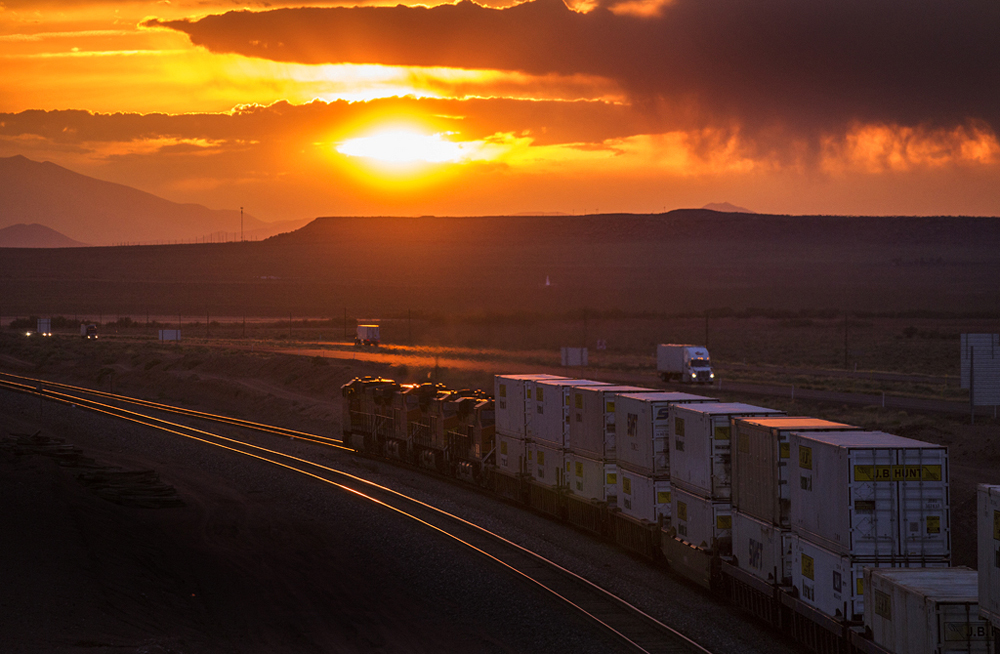 Train moving toward setting sun on line paralleling highway