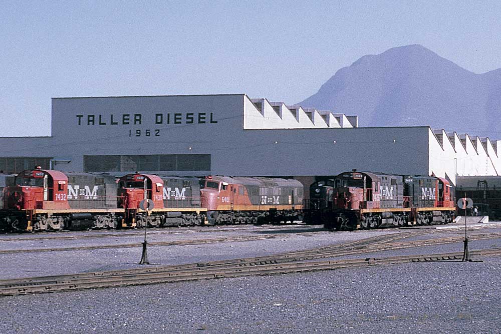 : Green and red diesel locomotives lined up outside immaculate shop building