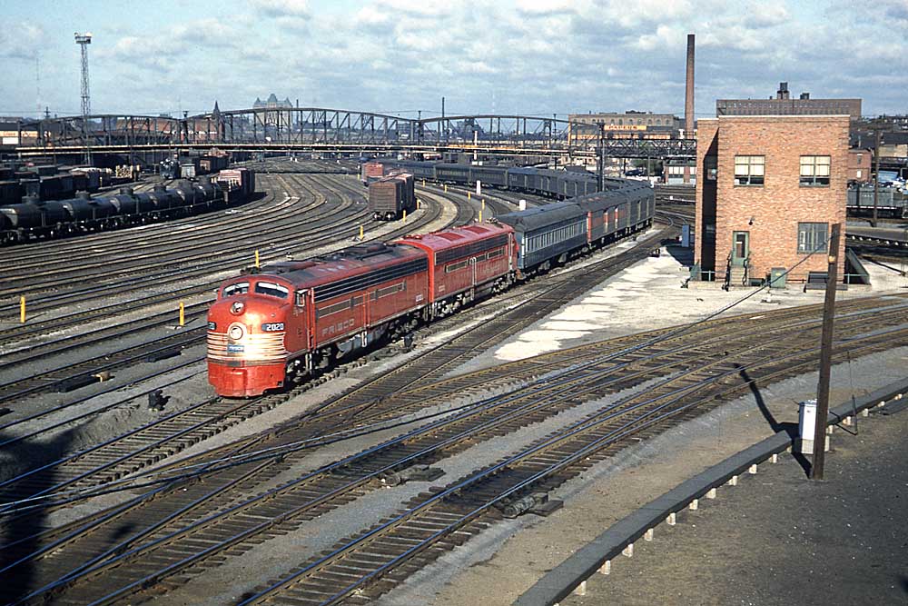 Yellow and gold streamlined diesel locomotives with passenger train on curve in yard