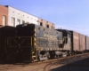 Black and gold diesel locomotives with Frisco freight train among industrial buildings