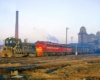 Black and yellow diesel locomotive pulls two red and yellow diesel locomotives and passenger cars