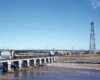 Black and gold diesel locomotives with Frisco freight train on low bridge