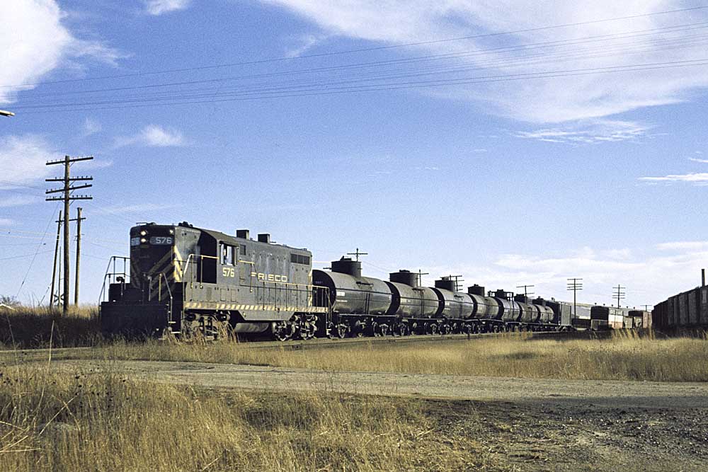 Black and gold diesel locomotive with Frisco freight train in tall grass