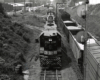 Above, head-on photograph of a black locomotive leading a long freight train forward the camera.