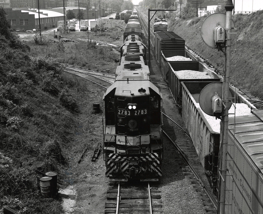 Above, head-on photograph of a black locomotive leading a long freight train forward the camera.