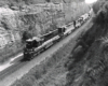 Black diesel locomotive leads a freigh train through a rock cut.